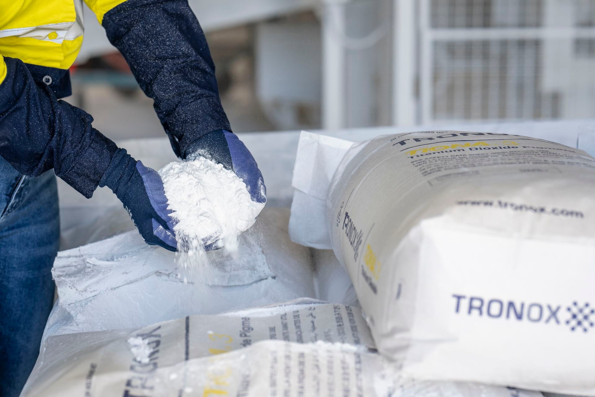 Person in gloves handling white powder next to Tronox-branded bags.